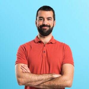 homem vestindo camisa polo vermelha com os bracos cruzados sobre fundo colorido